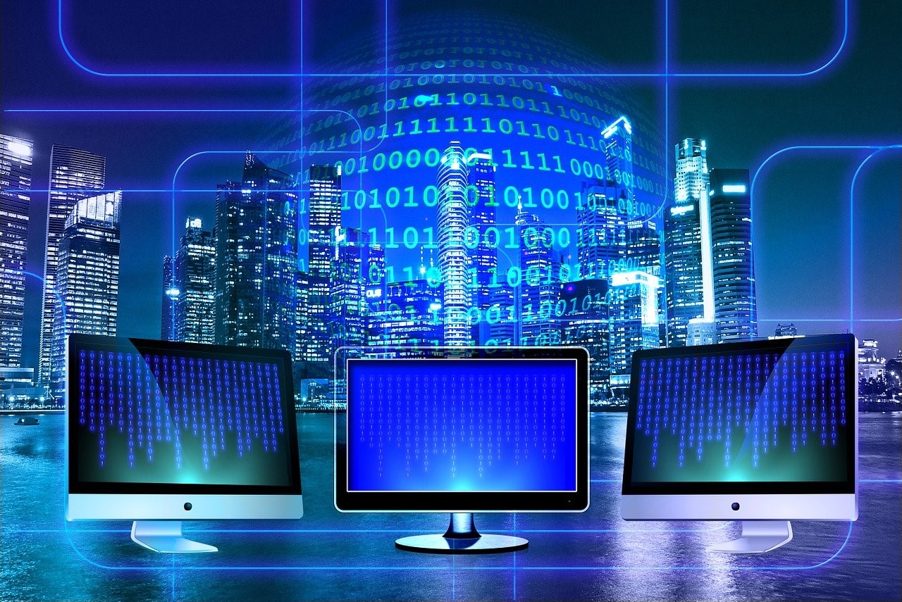 three computer monitors in front of city with binary code overlaid building